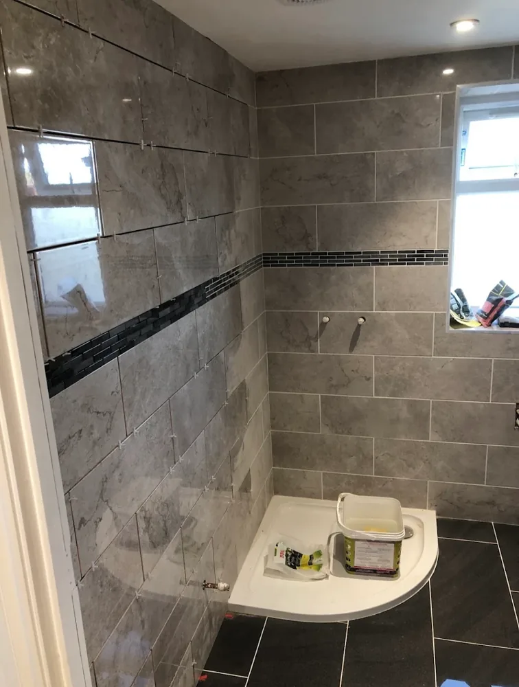 Bathroom renovation during tiling: grey marble-effect tiles with a mosaic border around a new shower